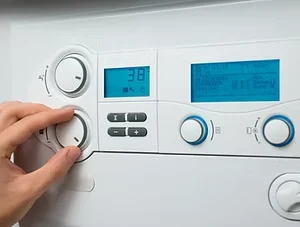Close-up of a hand adjusting the temperature dial on a modern gas combi boiler control panel